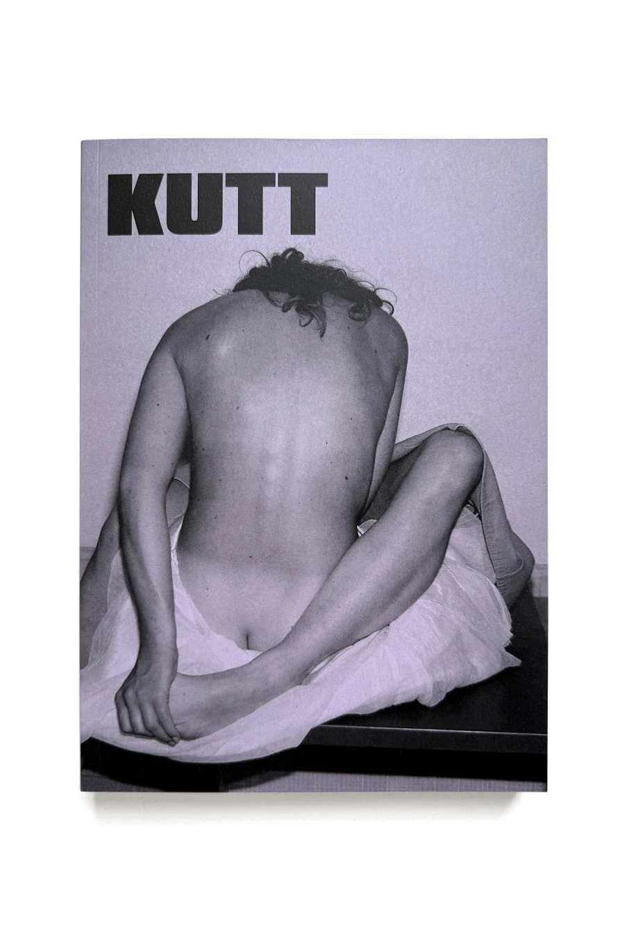A square art print or book cover featuring a black-and-white photograph of a seated nude figure from behind, with the word 'KUTT' in large bold letters at the top, shown against a white background.